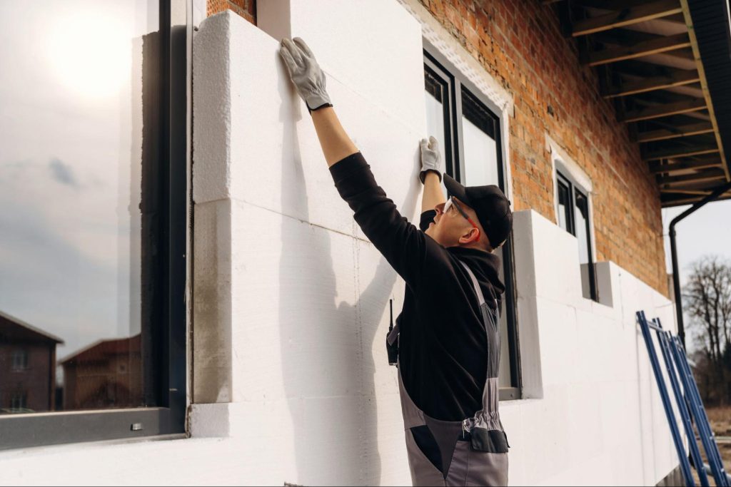 Vakman bevestigt witte isolatieplaten op de buitengevel van een bakstenen woning.
