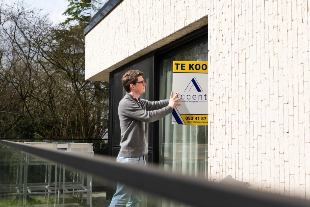 Makelaar van Immo AccentA plaatst een te-koop-bord bij een woning in Vlaanderen
