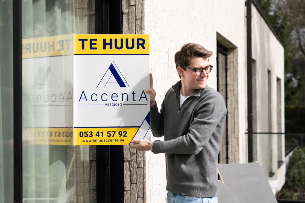 Vastgoedmakelaar van Immo AccentA hangt een te-huur-bord op aan een moderne woning.